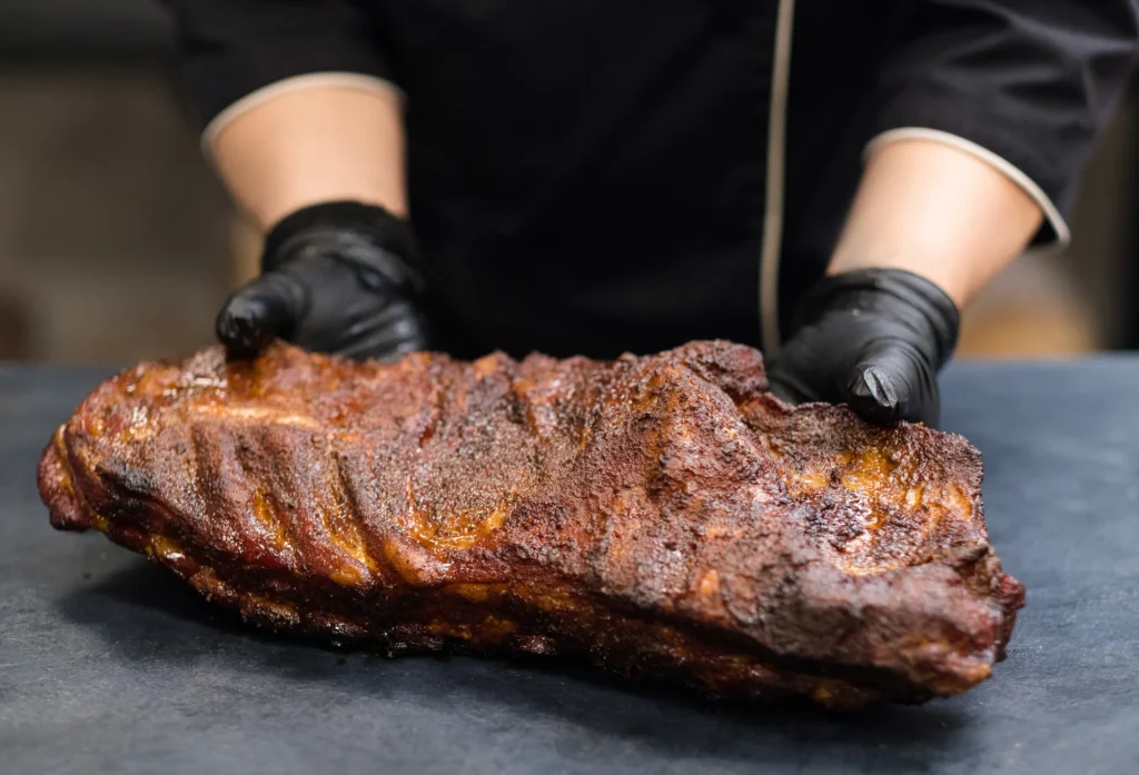 screenshot grill restaurant kitchen. closeup of chef hands in black cooking gloves holding smoked pork ribs 281762622